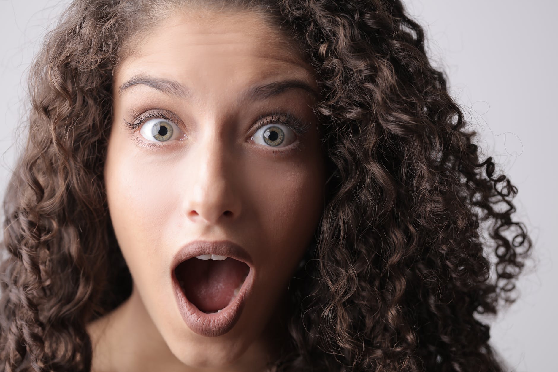 close up photo of shocked woman with brown curly hair