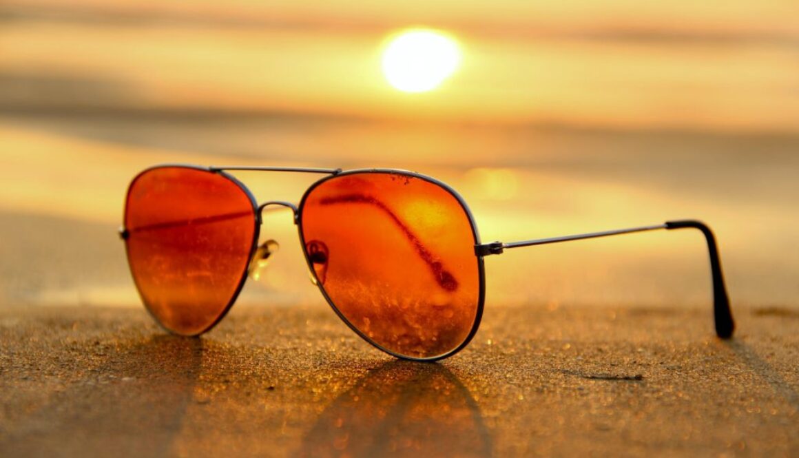 red lens sunglasses on sand near sea at sunset selective focus photography